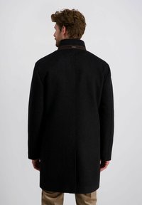 Schwarzer Wollmantel mit hohem Kragen, geradem Schnitt und verdeckten Knöpfen. Mit einem braunen Akzent am Kragen und langen Ärmeln.