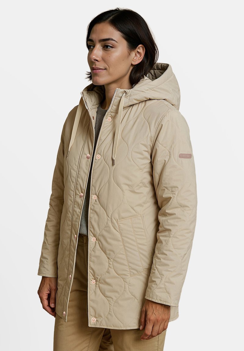 Beige gewatteerde jas met een capuchon, voorzien van roze drukknoopjes, een klepzak en gestructureerde golfpatronen op de stof.