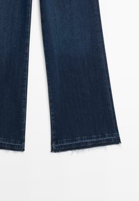 Ciemnoniebieskie, szerokie dżinsy z surowym wykończeniem; wykonane z bawełnianego materiału, charakteryzujące się gładką fakturą i klasycznym pięciokieszeniowym krojem.