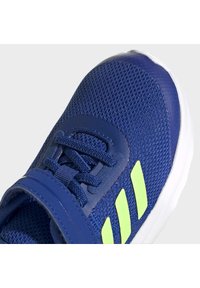 Scarpa sportiva blu con tomaia in rete, presenta dettagli verde lime, un colletto imbottito e una suola in gomma bianca. Lacci integrati per una vestibilità sicura.