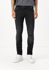 Jeans de mezclilla negros con un corte ajustado, que presentan un detalle desgastado en la rodilla y un estilo clásico de cinco bolsillos. Combinados con zapatillas blancas.