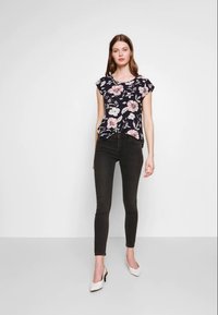 Blusa floral azul-marinho com mangas curtas, combinada com jeans skinny pretos e sapatos de salto alto brancos. Tecido suave, padrão floral, corte casual.