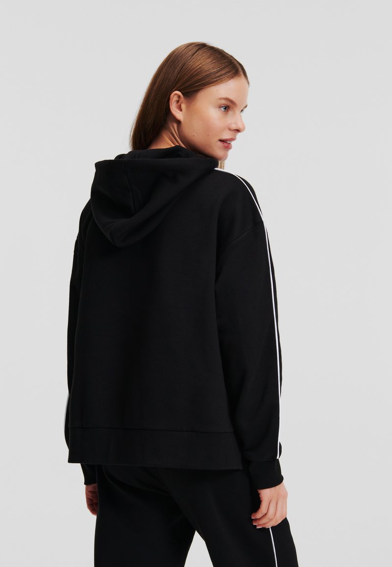 Schwarzer Kapuzenpullover mit weißen Seitenstreifen, lockerer Schnitt und gerippten Bündchen und Saum. Aus weichem, strukturiertem Stoff gefertigt.