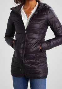 Chaqueta acolchada negra con cremallera al frente, capucha y bolsillos laterales. El material parece brillante y ligero, adecuado para el clima frío.