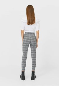 Leggings a vita alta, aderenti, con un motivo a quadri bianco e nero, abbinati a una camicia bianca con colletto decorato in pizzo.