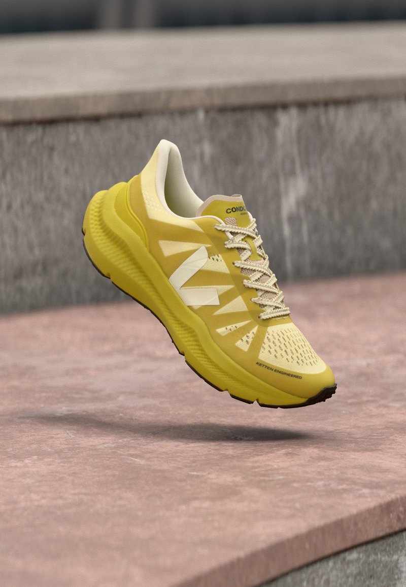Chaussure de sport jaune avec des accents blancs et des lacets beiges, flottant au-dessus d'une surface extérieure texturée rose et grise.