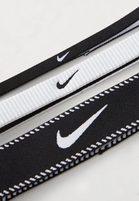 Tre elastiske remme: to sorte med hvide Nike-logoer og syninger, én hvid med ribbet tekstur, alle i en flad arrangement.