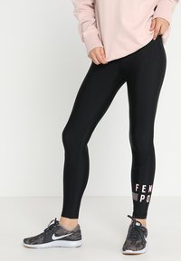 Henkilö, joka on pukeutunut mustiin legginsseihin ja vaaleanpunaiseen ylisuurta collegepaitaan, seisoo niin, että toinen jalka on hieman eteenpäin, esitellen urheilukenkiään, joissa on erityinen muotoilu.