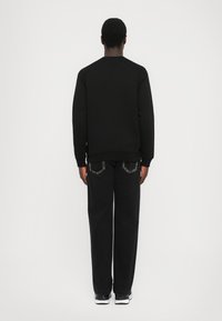 Črna majica s krožnim izrezom in rebrastimi manšeti, v kombinaciji s črnimi širokimi hlačami, ki imajo edinstvene vzorčaste zadnje žepke.