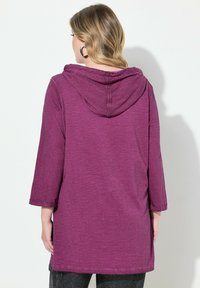 Violetti pitkähihainen huppari, jossa on tekstuuri ja löysä istuvuus, takana huppuja ja käärityt hihansuut.