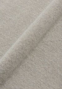 Hellgrauer Stoff mit einer weichen, strukturierten Oberfläche, der ein feines Strickgewebe und einen dezenten Glanz aufweist. Das Material wirkt warm und gemütlich.