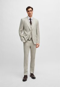 Lys grå tre-delt dress med pyntet skjortekrage, dobbeltspent vest og slim-fit bukser. Kombinert med mørkebrune sko.