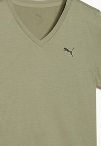 Olivno zelena v-neck majica iz mehke tkanine. Ima majhen črn Puma logotip na levi strani prsnega koša. Gladka tekstura, preprost dizajn.