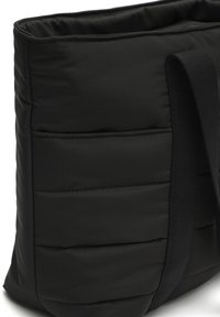 Čierna vystlaná taška so štvorcovým tvarom a jemnou textúrou. Má široký popruh a niekoľko vonkajších vreciek.