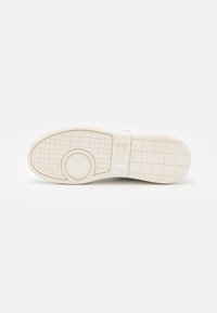 Sole di sneaker bianca con un motivo a griglia testurizzata e un accento circolare. Il materiale sembra gomma con un dettaglio del logo leggermente in rilievo.