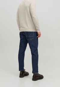 Beige, långärmad stickad tröja med rund halsringning, kombinerad med mörkblå denimjeans som har två bakfickor. Svarta skor fulländar looken.
