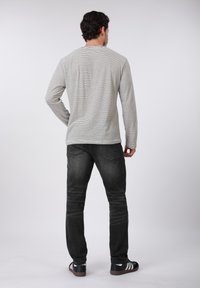 Γκρι και λευκό ριγέ μακρυμάνικο πουκάμισο, σκουρόχρωμο τζιν στενής γραμμής και μαύρα αθλητικά παπούτσια με λευκές ρίγες, με θέα από πίσω.