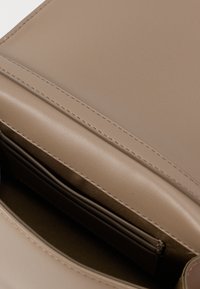 Bežs ādas rokassoma ar gludu virsmu, smalku šuvumu un vienu nodalījumu, kas aprīkots ar iekšējām kabatām organizācijai.