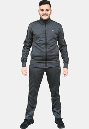 Chándal gris oscuro con chaqueta con cremallera y pantalones a juego. Textura suave, corte ajustado, con un logo en el pecho y rayas laterales.