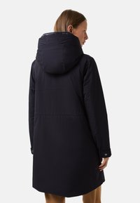 Granatowy długi płaszcz z kapturem, charakteryzujący się gładką teksturą, zatrzaskami i średniej długości krojem. Widok z tyłu ukazuje szwy i styl.