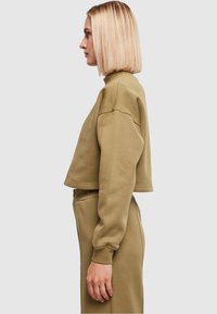 Felpa corta verde oliva con collo alto, polsini a coste e tessuto morbido. Abbinate a pantaloni a vita alta coordinati.