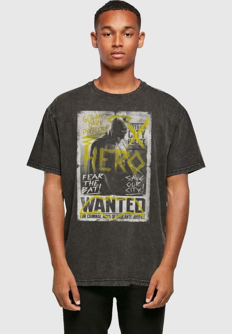 Camiseta negra de gran tamaño con un diseño gráfico de un cartel de Se Busca, con texto y acentos amarillos, que muestra una silueta oscura y tipos de letra en negrita.