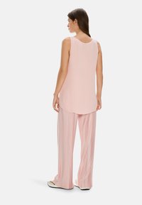 Light pink sleeveless top with a rounded neckline, paired with wide, pleated light pink trousers. Smooth texture, relaxed fit, minimal design.