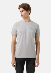 Grå T-shirt med korte ærmer i et glat stof med rund hals. Har et diskret logo på venstre bryst og et rent, minimalistisk design.