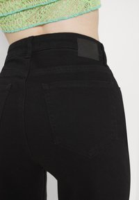 Zwarte denim jeans met een soepele textuur, voorzien van twee achterzakken en een zwart leren label op de taille. Geen zichtbare versieringen.