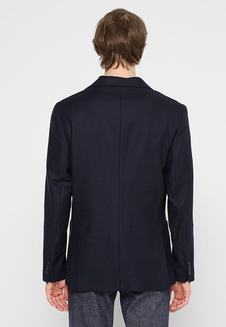 Granatowa marynarka z usztywnionymi ramionami, pojedynczym rozcięciem z tyłu i dwoma guzikami na mankietach. Gładki, dopasowany materiał z czystym, minimalistycznym wzornictwem.