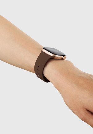 Muñeca con un reloj inteligente de oro rosa con pantalla negra y correa de silicona marrón oscuro sobre un fondo gris liso.