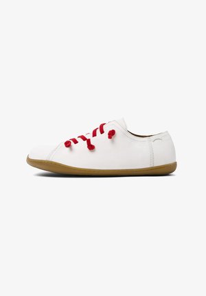 White canvas sneakers with red laces, rounded toe, low-cut design, and natural rubber sole. Minimalist style with stitched accents.