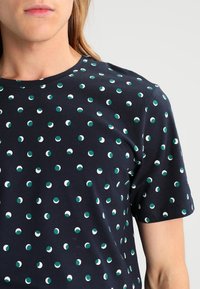 Camiseta de manga corta en color azul marino con un patrón de pequeños puntos verdes y blancos. Tejido de algodón suave con cuello redondo.