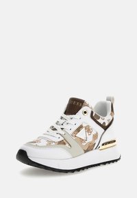 Zapatilla blanca con acentos marrones, herrajes dorados y un diseño estampado. Presenta una suela negra gruesa y un cuello acolchado para mayor soporte.