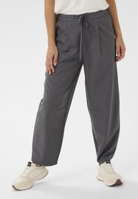 Pantalon gris à jambes larges avec taille à cordon, deux poches latérales et tissu léger. Assorti à des baskets beiges.