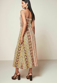 Maxime dress, joka esittelee monivärisiä geometrisia kuvioita, rypytettyä vartaloa ja leveää hametta. Yhdistetty ruskeisiin lohkare-korkoisiin sandaaleihin.