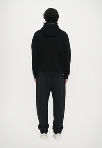 Felpa nera con cappuccio, polsini e orlo a coste. Abbinata a pantaloni neri larghi e sneakers bianche. Design semplice e minimal.