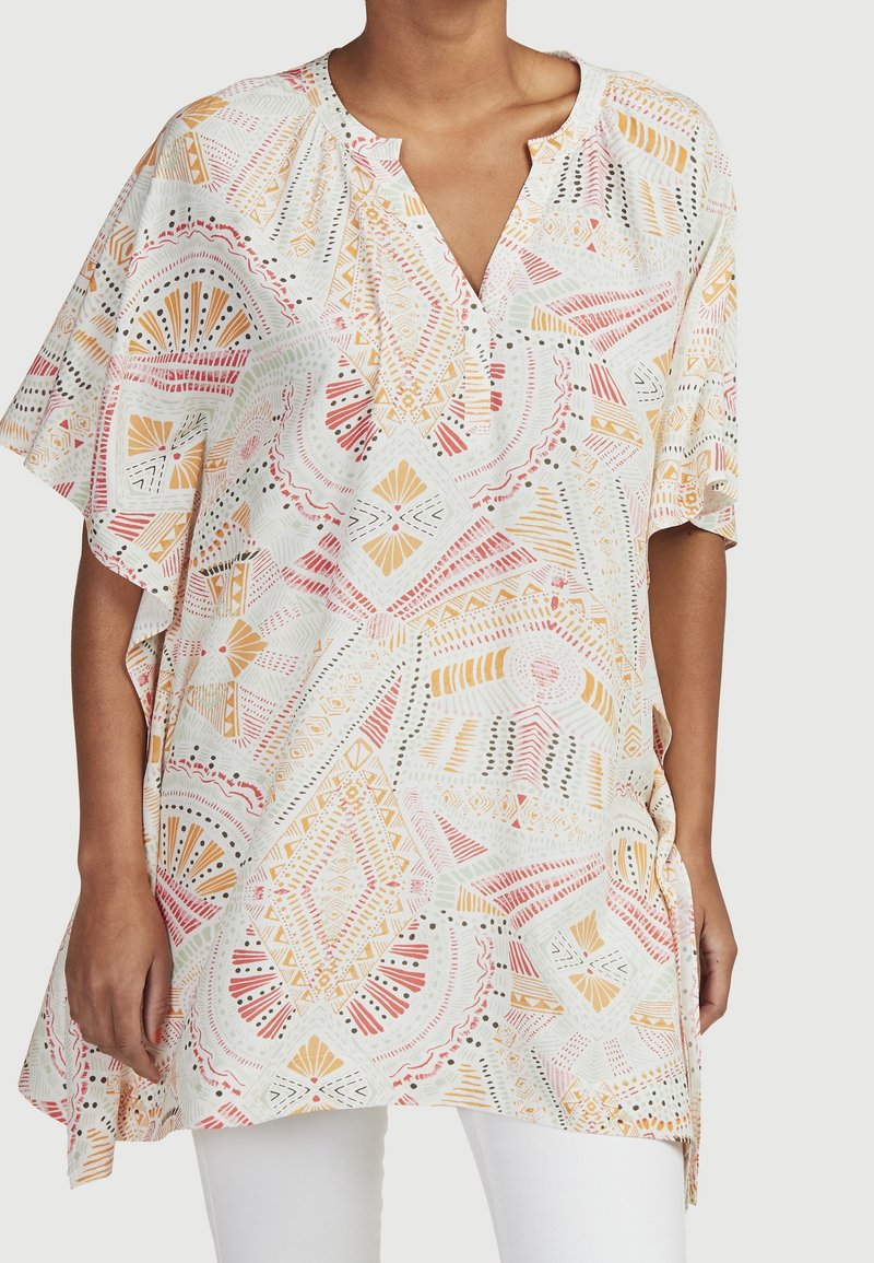 Lätt, mönstrad tunika med V-ringning och korta ärmar, med geometriska former i rosa, orange och grönt på en vit bakgrund.