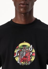 Black short-sleeve t-shirt featuring a colorful graphic of a skeleton in a sombrero, adorned with roses, holding food and drink.