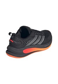 Μαύρο αθλητικό παπούτσι με υφασμάτινο επάνω μέρος με υφή, που διαθέτει τρεις ασημένιες ρίγες, μαξιλαρωμένη πορτοκαλί σόλα και θηλιά στο πίσω μέρος για εύκολο φόρεμα.