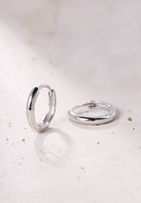 Orecchini a cerchio in argento con superficie liscia e lucida, caratterizzati da un design senza soluzione di continuità e forma arrotondata. Due orecchini mostrati su uno sfondo neutro.