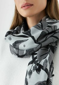 Écharpe à motifs floraux noirs et gris en tissu léger, drapée autour du cou, avec une texture lisse et un léger éclat.