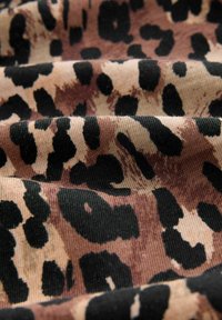 Tessuto animalier con macchie nere su uno sfondo marrone chiaro, che mette in mostra una consistenza morbida e leggere variazioni di colore e motivo.