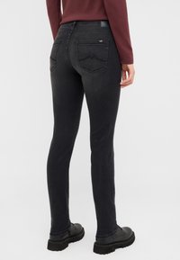 Czarne dżinsy o slim fit, z tylnymi kieszeniami i gładką teksturą, zestawione z czarnymi sznurowanymi butami.