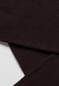 Tejido de color marrón oscuro, con un tejido texturizado y fibras visibles, bordes doblados, área de superficie lisa que indica una calidad textil suave.
