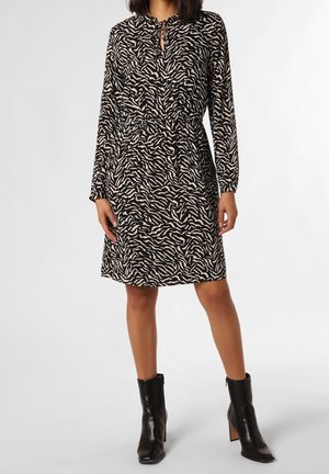 Femme portant une robe zébrée noire et beige mi-longue avec des manches longues et un décolleté en trou de serrure, associée à des bottines noires.