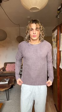 Lila csíkos hosszú ujjú pulóver kerek nyakkivágással. Az anyag puhanak és texturáltnak tűnik, világosszürke melegítőnadrággal párosítva.