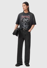 Zwart grafisch t-shirt met een ontwerp van een schedel en slang, gecombineerd met zwart, hoog getailleerd spijkerbroek en een zwarte riem. Minimalistische accessoires.