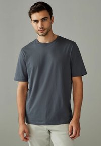 Mørkegrå bomulds t-shirt med korte ærmer, rund halsudskæring og en glat tekstur, båret med lyse bukser. Ingen synlige mønstre.