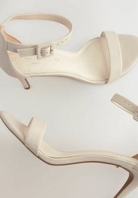 Sandalias de tacón alto beige con acabado texturizado, correa en el tobillo ajustable y tira delantera lisa. Tacón delgado y plantilla acolchada.